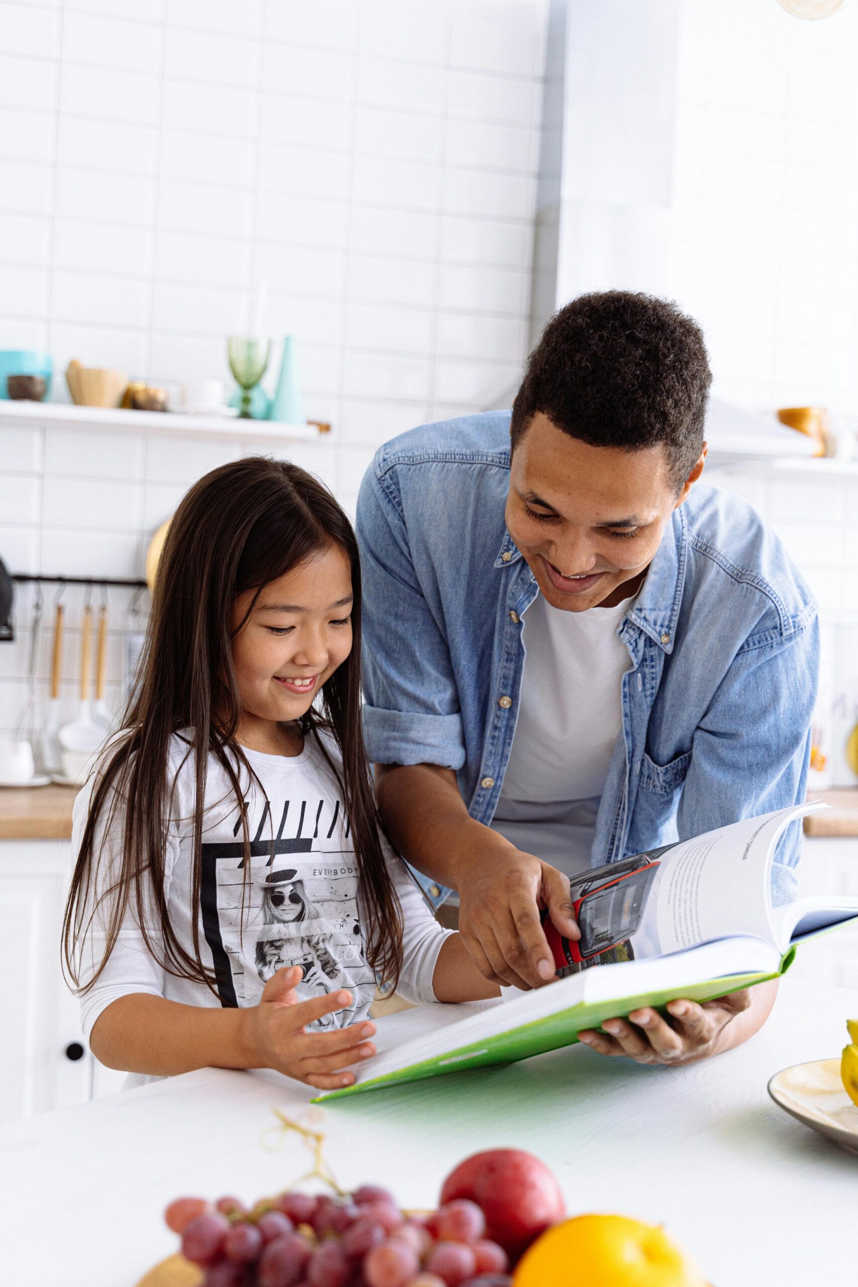 A father and his young daughter enjoy reading a book together in their home kitchen.